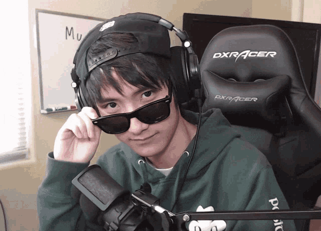 a young man wearing sunglasses and headphones is sitting in a dxracer chair