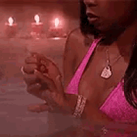 a woman in a pink bikini is sitting in a hot tub with candles in the background .