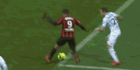 a soccer player is kicking the ball while another player is laying on the field .