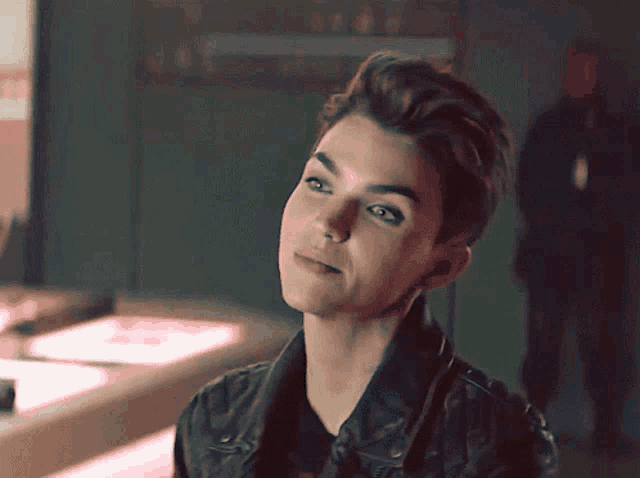 a woman with short hair and a leather jacket looks to the side