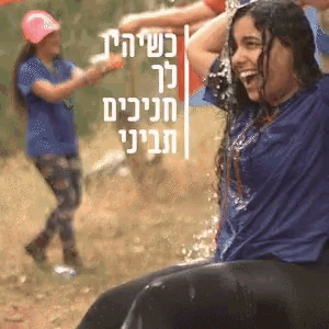 a woman in a blue shirt is laughing while being sprayed with water