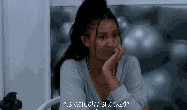 a woman is sitting in a chair with her hand on her face and the words " is actually shocked " written on the bottom