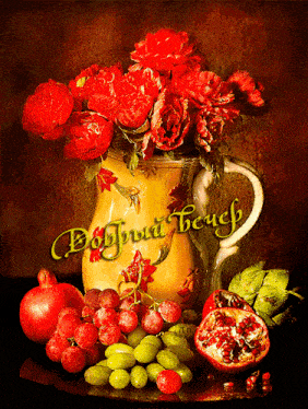 a vase of red roses sits next to grapes and pomegranates on a table