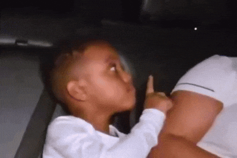 a little boy is sitting in the back seat of a car holding his finger to his mouth .