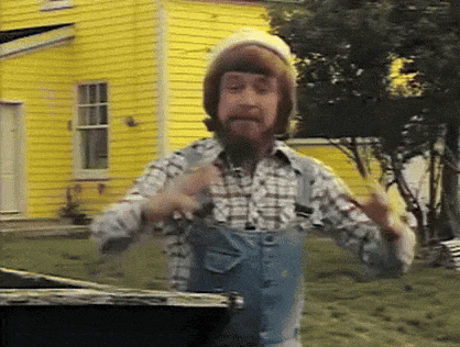 a man with a beard wearing overalls and a hat is standing in front of a yellow house