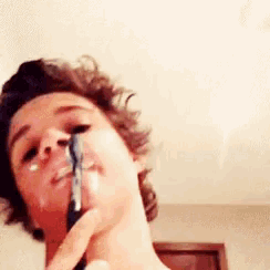a young man shaving his face with a razor