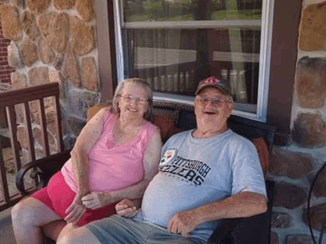 a man and a woman are sitting on a porch holding hands and smiling .