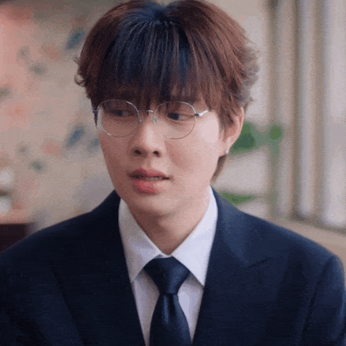 a young man wearing glasses and a suit is looking at the camera