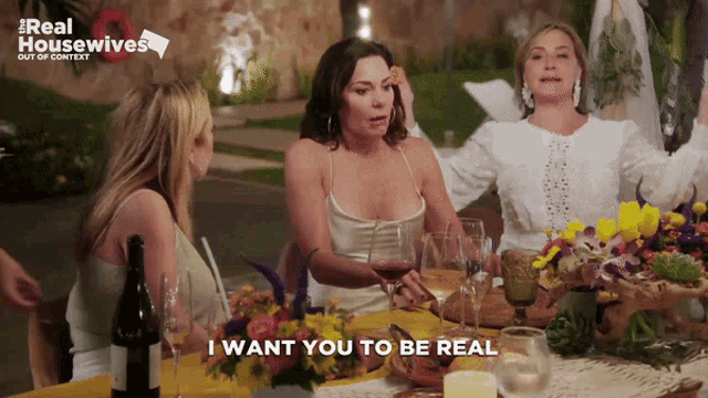 a group of women are sitting at a table with flowers and wine glasses and one of them says i want you to be real