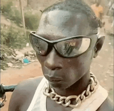 a man wearing sunglasses and a gold chain around his neck is making a funny face .
