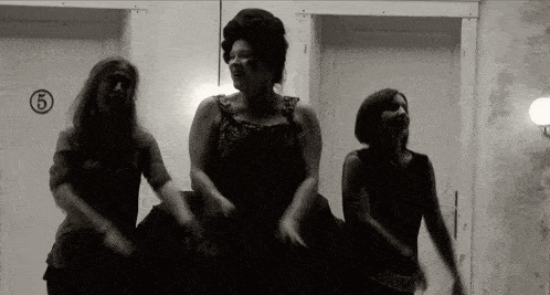 a black and white photo of three women dancing in front of a door with the number 5 on it