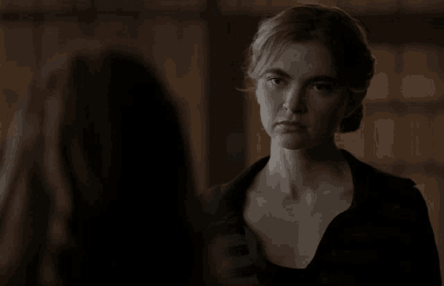 a woman in a black shirt is looking at another woman in a dark room