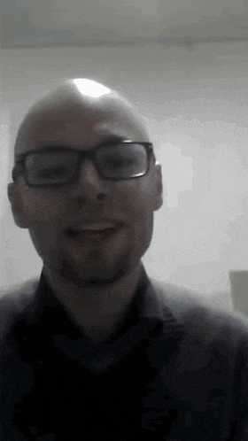 a bald man with glasses and a beard is smiling in a dark room .