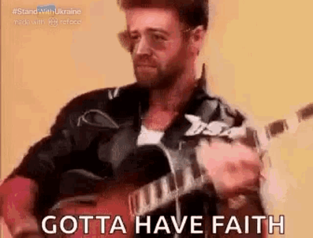 a man is playing a guitar with the words `` gotta have faith '' written on it .