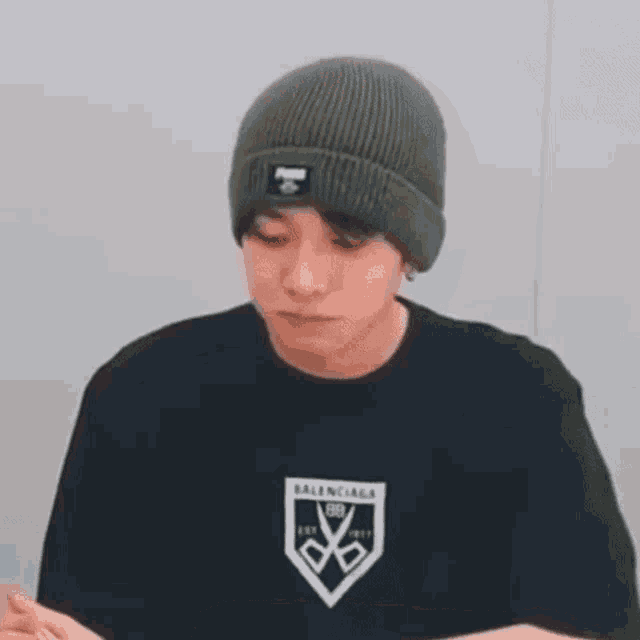 a man wearing a beanie and a balenciaga t-shirt is looking at the camera .