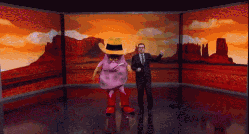 a man in a suit and tie stands next to a mascot in a cowboy hat and boots