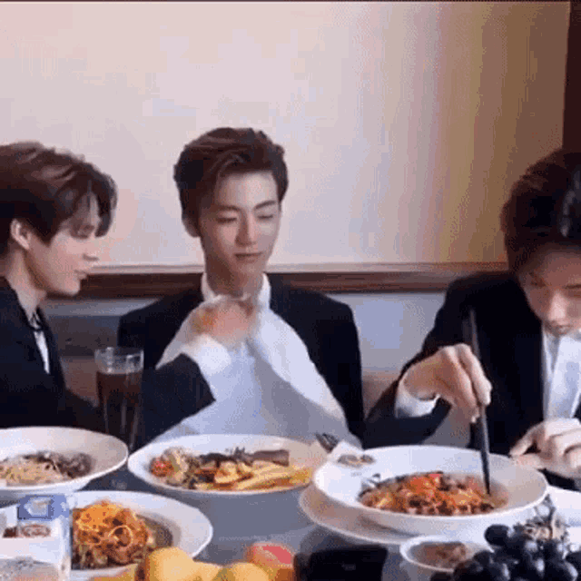 a group of men are sitting at a table eating food with chopsticks .