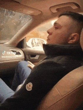 a man in a moncler jacket is sitting in the driver 's seat of a car ..