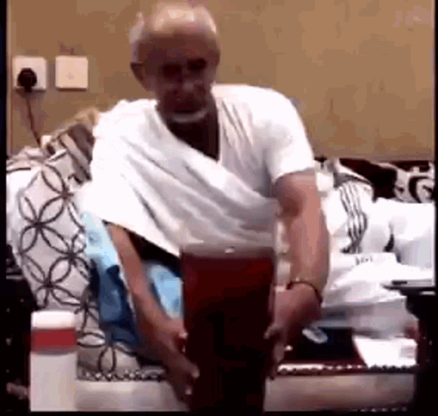 a man in a white shirt is sitting on a couch holding a glass .