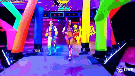 a couple of women are standing on a stage in front of a neon colored wall .
