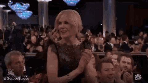a woman in a black dress is applauding at a golden globes event