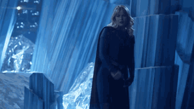 a woman in a cape stands in front of a wall of ice