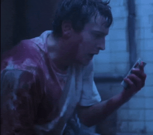 a man in a bloody shirt is looking at a cell phone