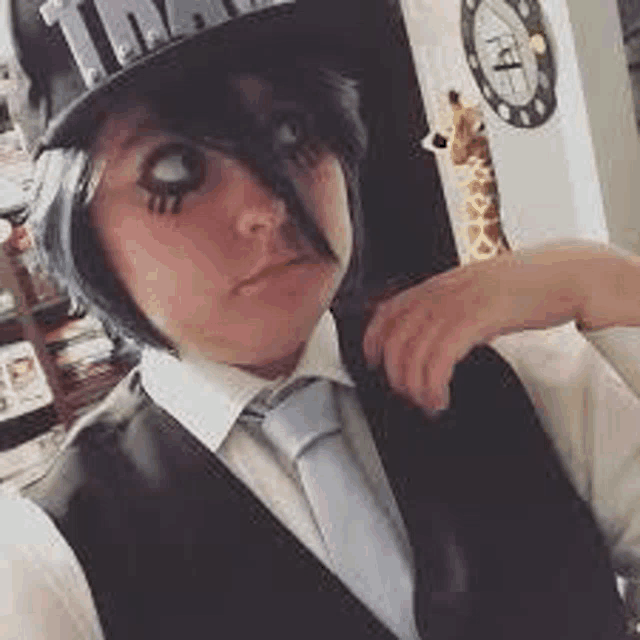 a person wearing a top hat , vest and tie is taking a picture of themselves .