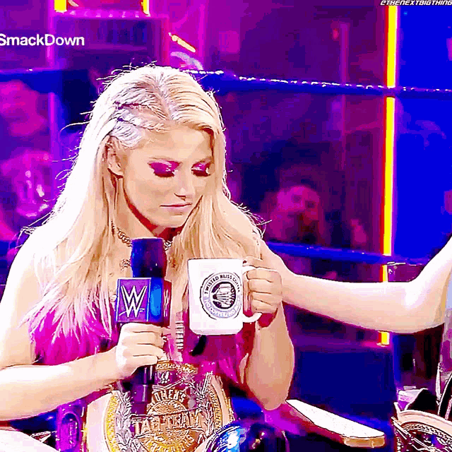 a woman in a wrestling ring holding a cup and a microphone with the word smackdown on the bottom