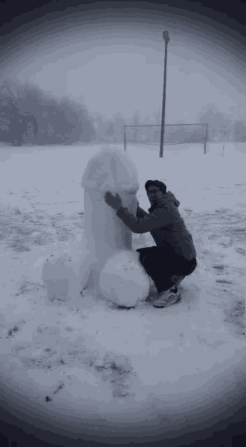 a man is kneeling down next to a snowman shaped like a penis .