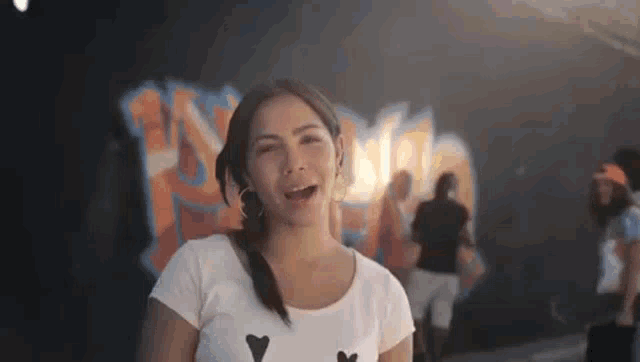 a woman in a white shirt is standing in front of a wall with graffiti on it .