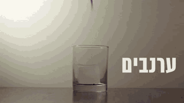 a glass of water is being poured into another glass with hebrew writing on the bottom
