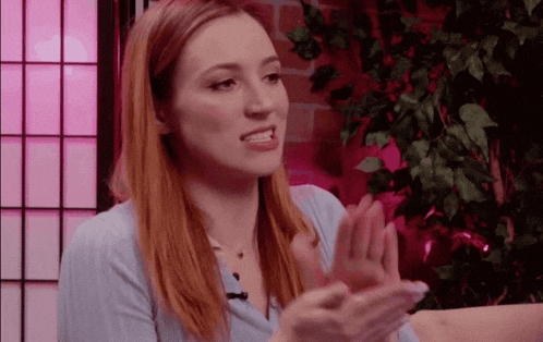 a woman clapping her hands in front of a pink screen