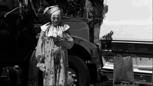 a black and white photo of a clown standing in front of a truck
