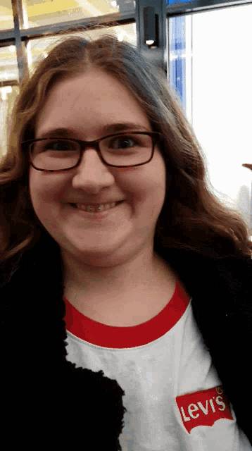 a woman wearing glasses and a white levi 's shirt smiles for the camera