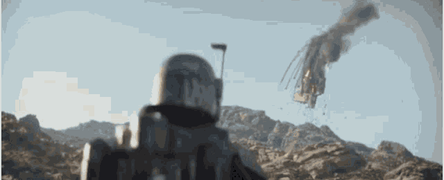 a man in a helmet is standing in the desert looking at a rocket flying through the air .