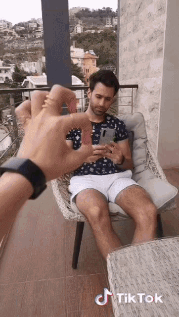 a man sitting on a balcony looking at his phone with a tik tok watermark