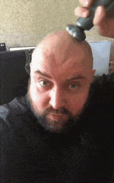 a bald man with a beard is shaving his head with a razor