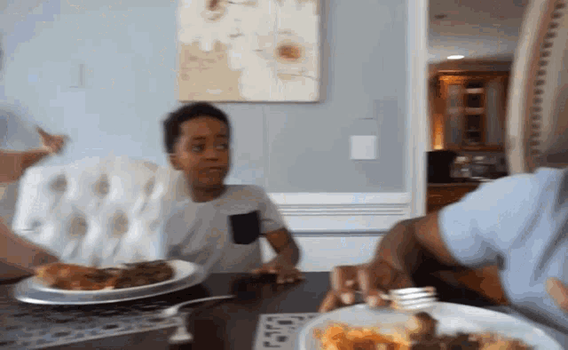 a boy sitting at a table with a plate of food and a fork