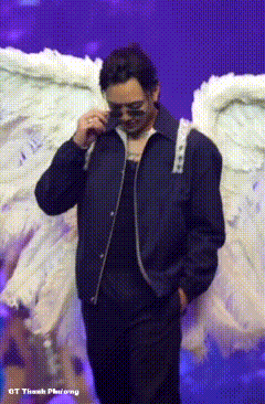 a man wearing sunglasses and a black jacket is standing on a stage with white angel wings