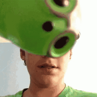 a woman in a green shirt is holding a green object in front of her head .