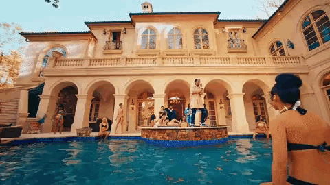 a group of people are standing around a swimming pool in front of a mansion .