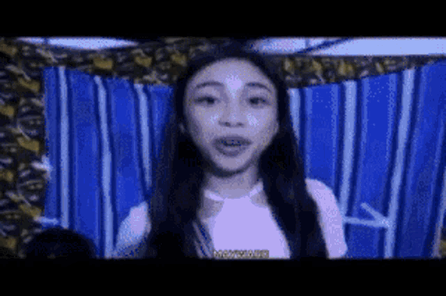 a girl with braces on her teeth is standing in front of a blue and white striped curtain