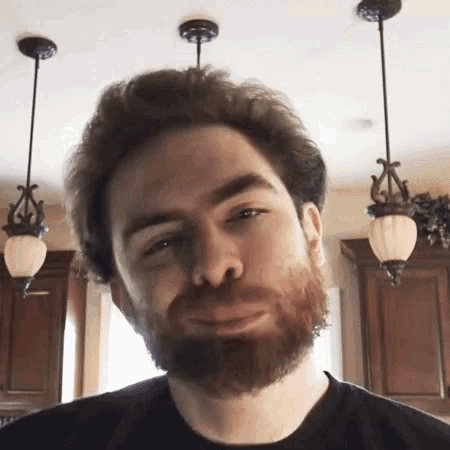 a man with a beard is making a funny face in a kitchen with hanging lights .