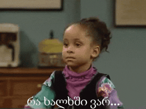 a little girl is wearing a purple sweater and a black vest with a foreign language on it
