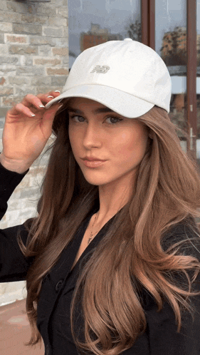 a woman wearing a white new balance hat looks at the camera