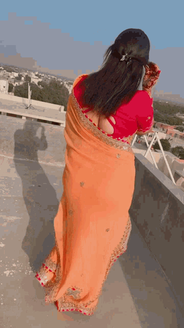 a woman wearing an orange saree and a red blouse is standing on a rooftop