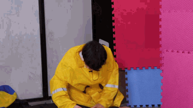 a man in a yellow raincoat sits on the floor next to a pink and blue puzzle mat