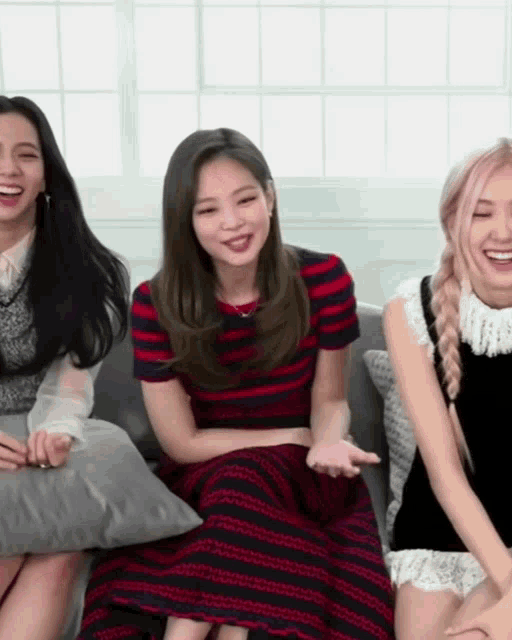 three women are sitting on a couch with pillows and smiling