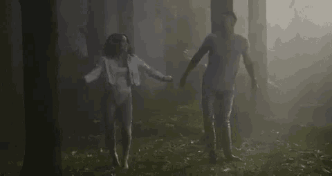 a man and a woman are dancing in a foggy forest at night .